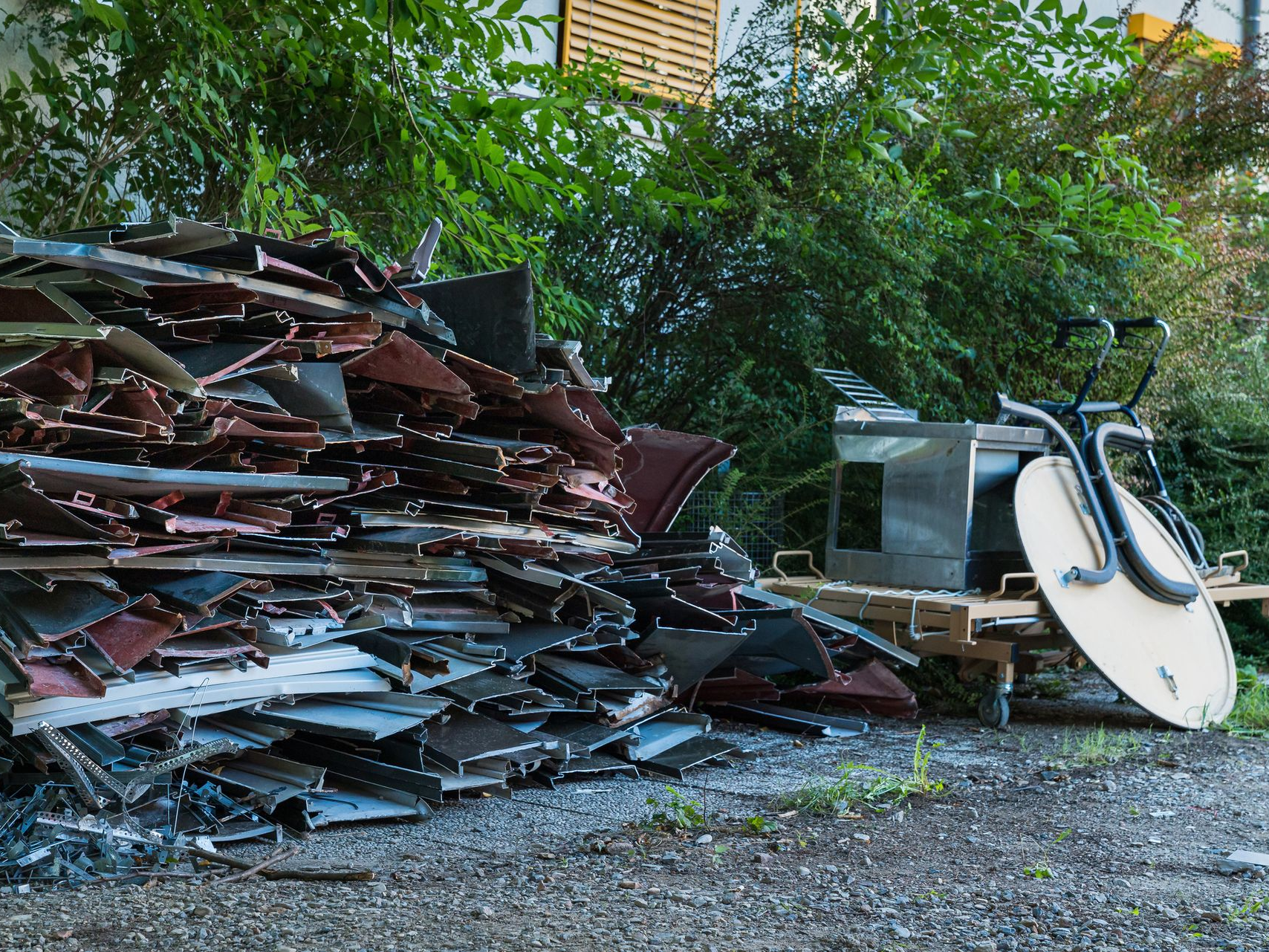 Pile of scrap metal and a cart against greenery on gravel. Pile of scrap metal and a cart against greenery on gravel.
