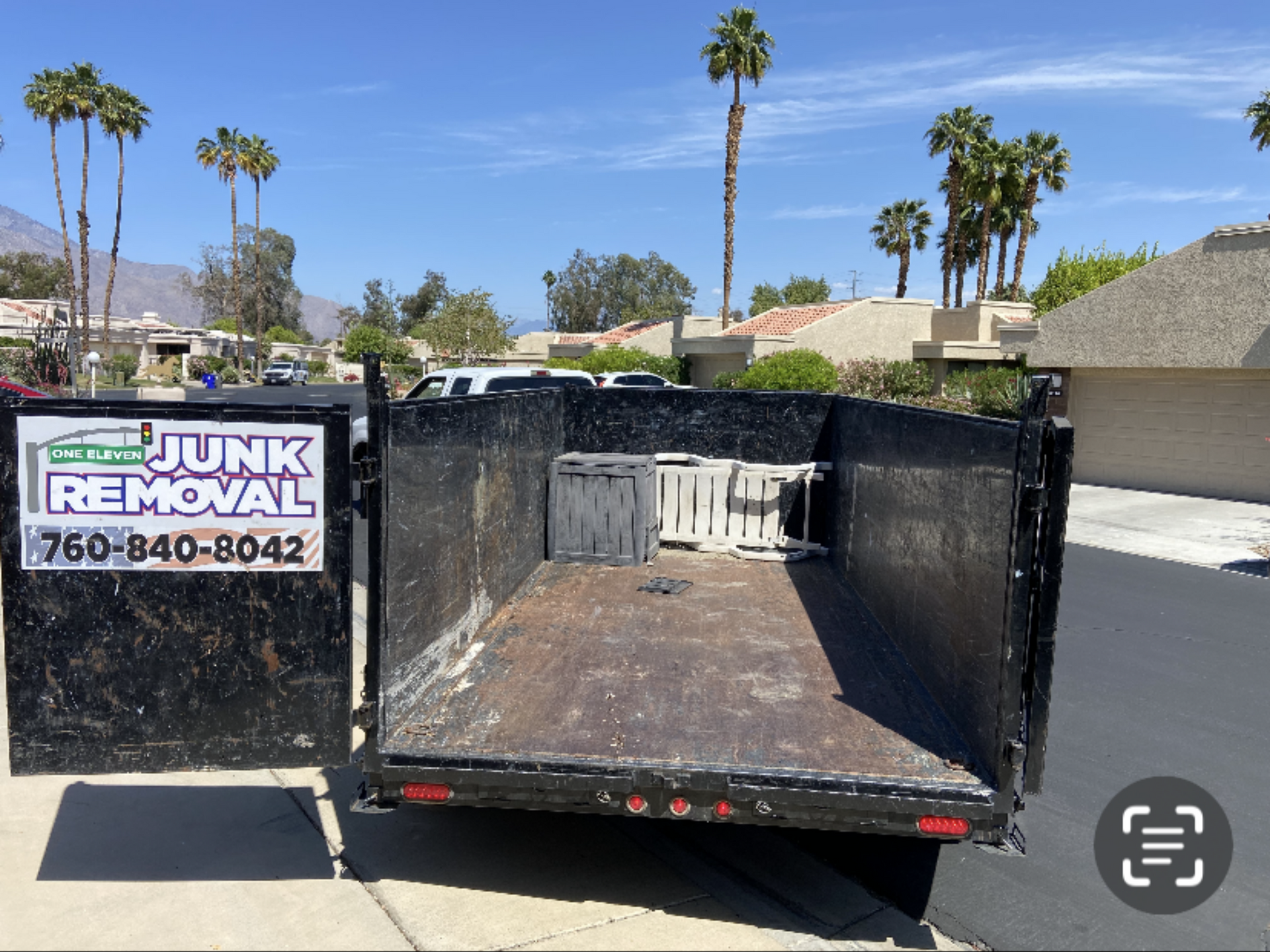 Open empty dumpster on a sunny day with palm trees and homes in the background. Open empty dumpster on a sunny day with palm trees and homes in the background.