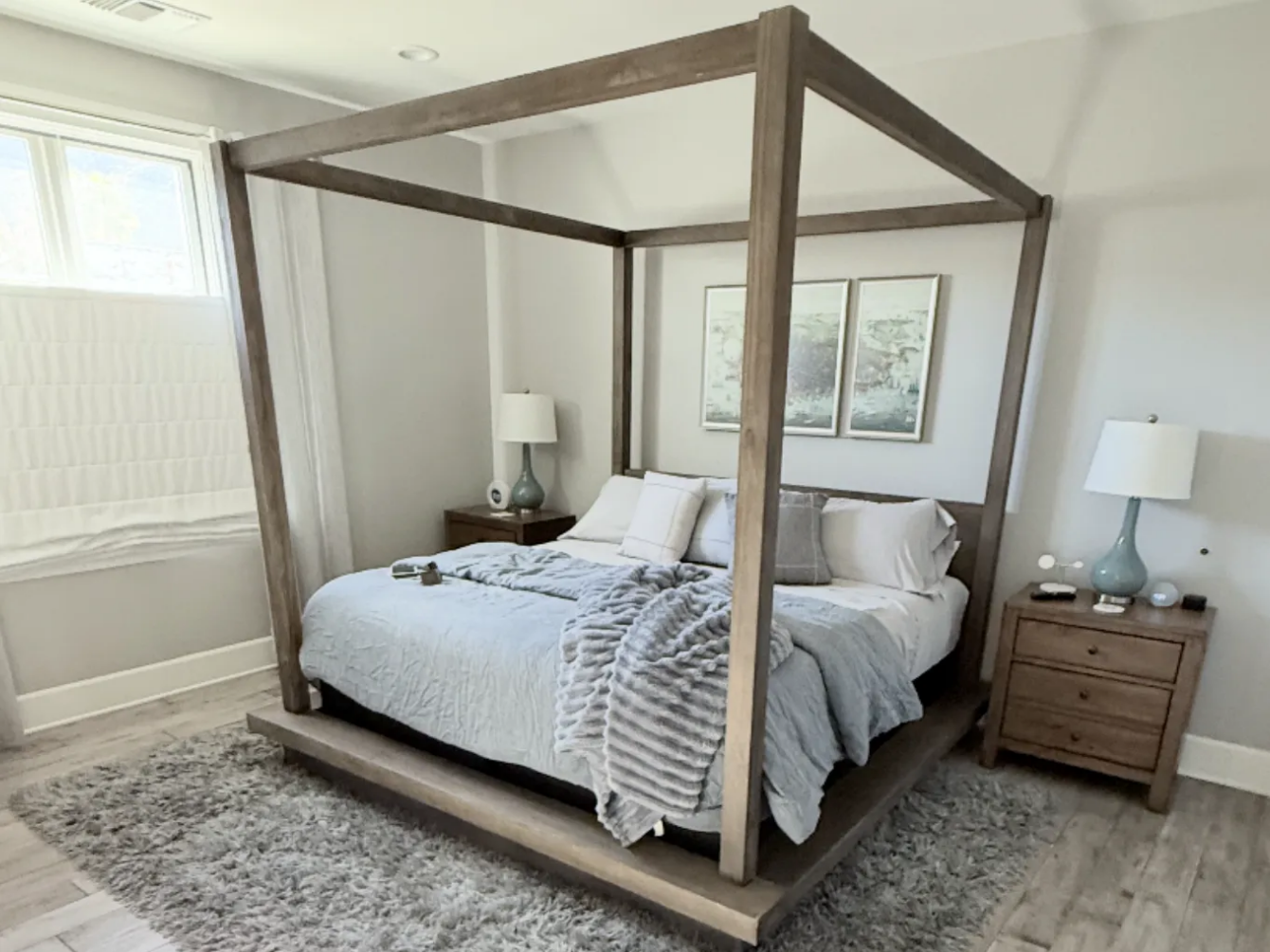 Bedroom with gray canopy bed, nightstands, and light gray bedding. Rug and window seat visible.