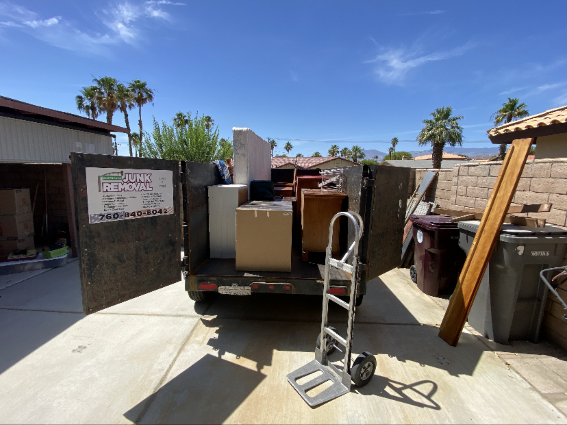 Trailer loaded with furniture; hand truck in foreground; sunny backyard setting. Trailer loaded with furniture; hand truck in foreground; sunny backyard setting.