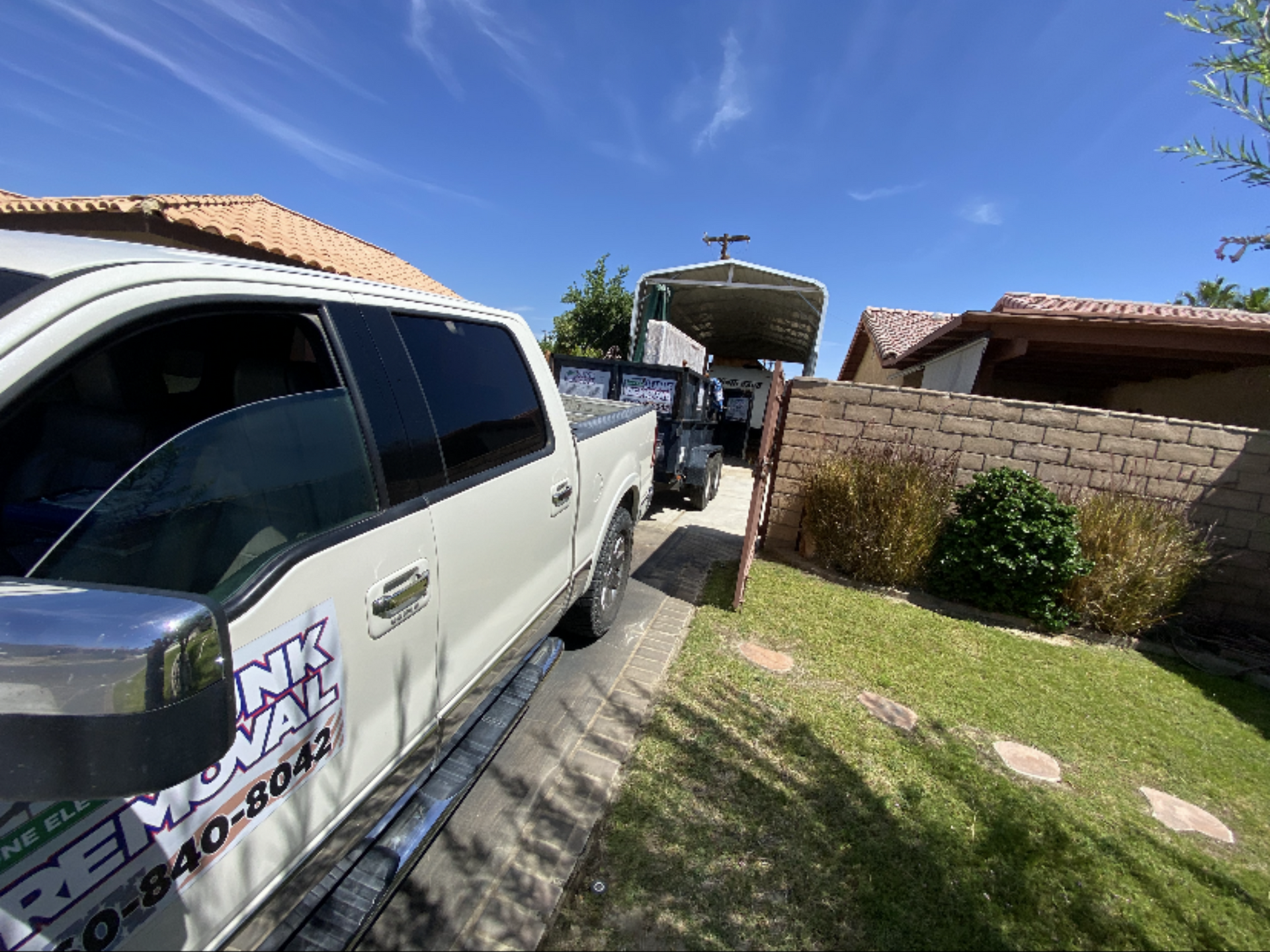 White truck pulling a trailer in a driveway, next to a house with red roof and brick wall, sunny day. White truck pulling a trailer in a driveway, next to a house with red roof and brick wall, sunny day.