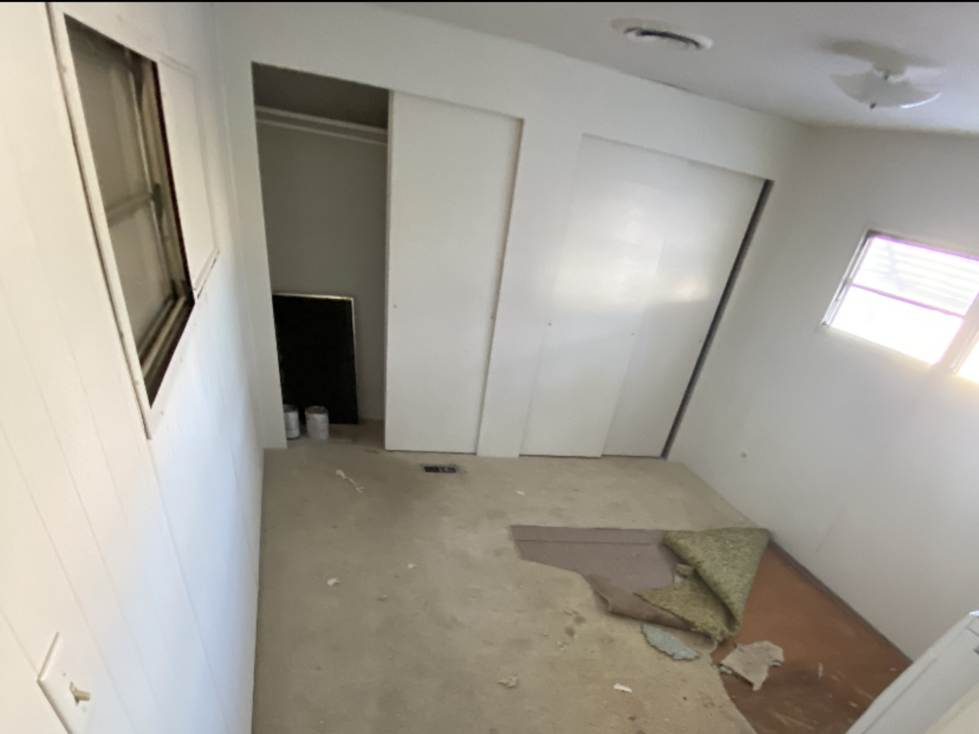 Empty bedroom with white walls, closet, small windows, and worn carpet. Empty bedroom with white walls, closet, small windows, and worn carpet.