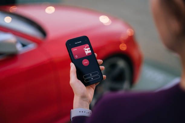 A person is holding a cell phone in front of a red car.