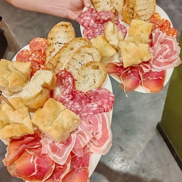 Tartare di tonno su piatto bianco, guarnita con fette d'arancia, verde e menta, con bottiglie sullo sfondo.