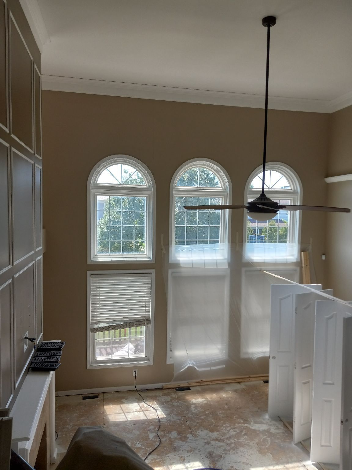 Interior view of a room with three arched windows, beige walls, a ceiling fan, and white trim.