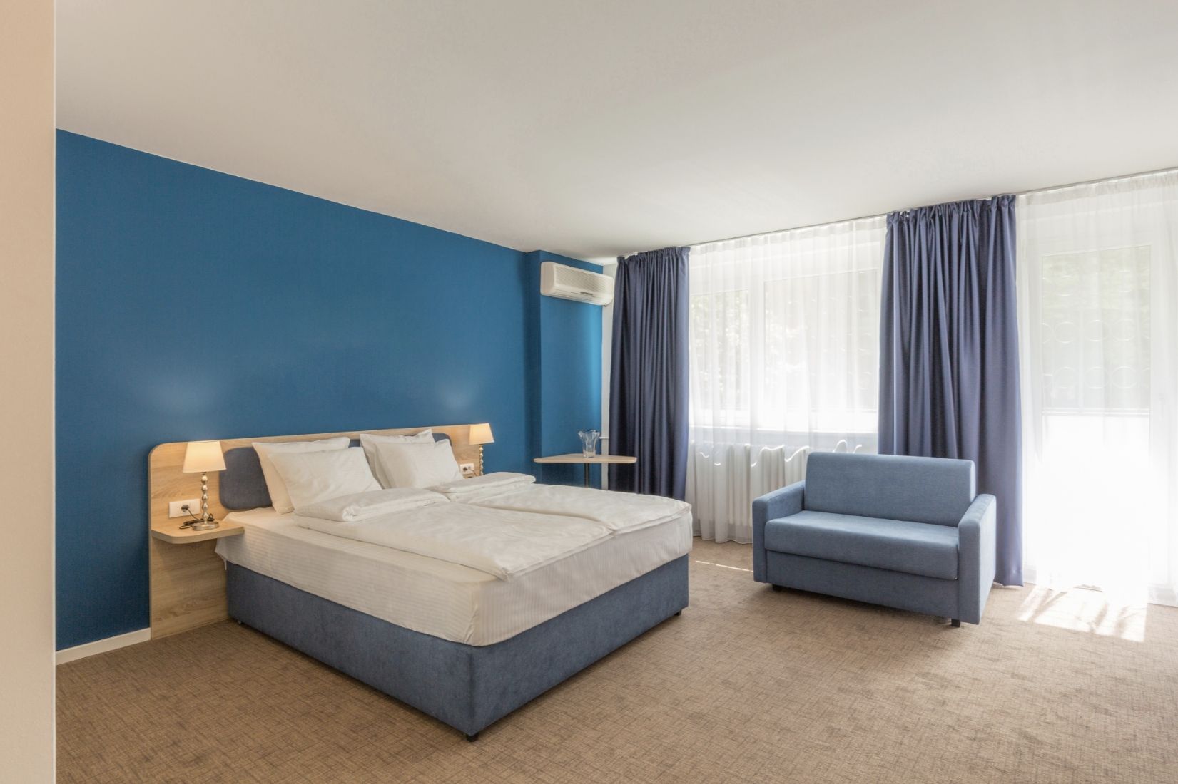 Hotel bedroom with blue accent wall, bed, sofa, and curtains.