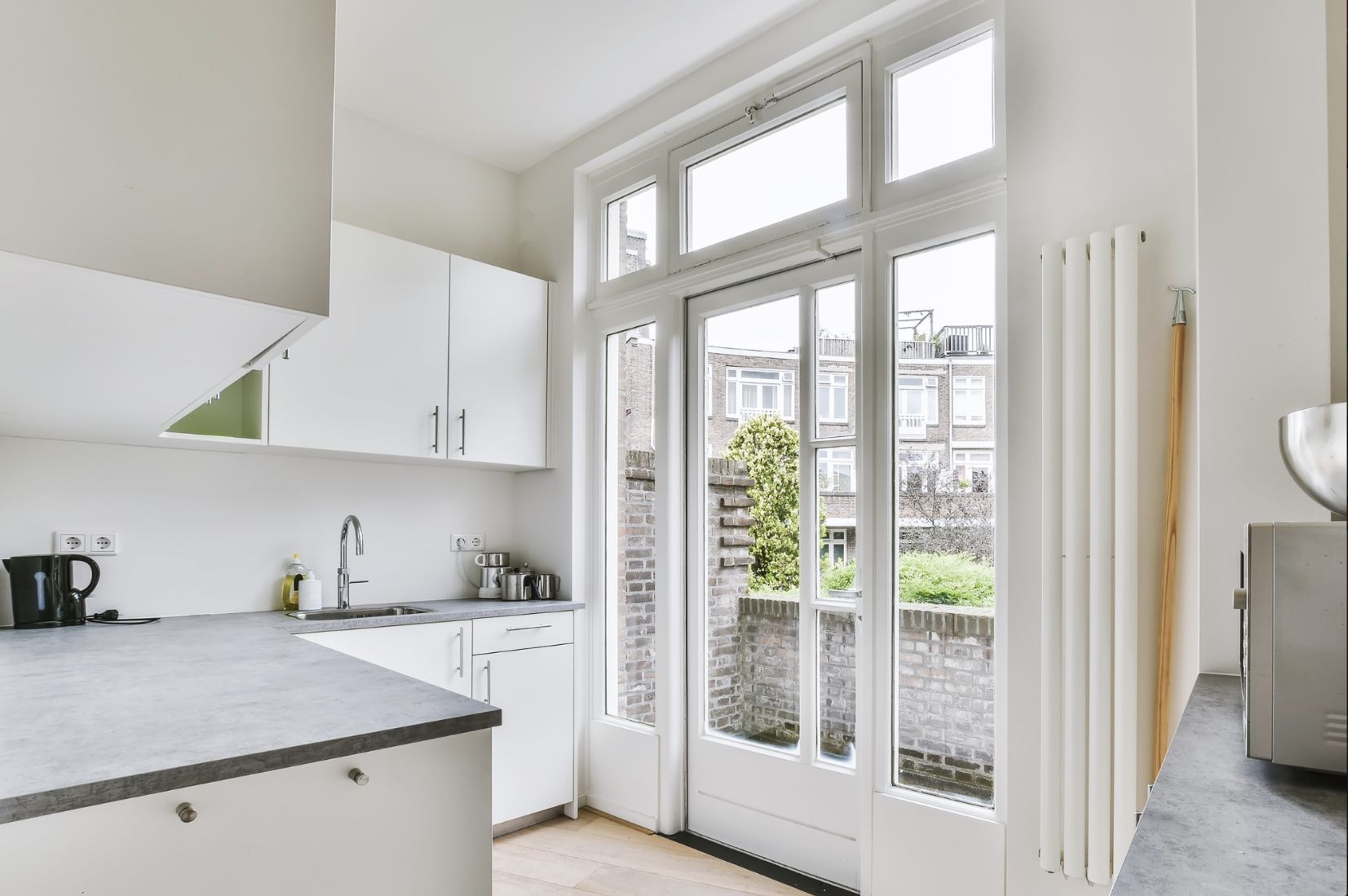 White kitchen with sink, cabinets, and a window overlooking a garden.