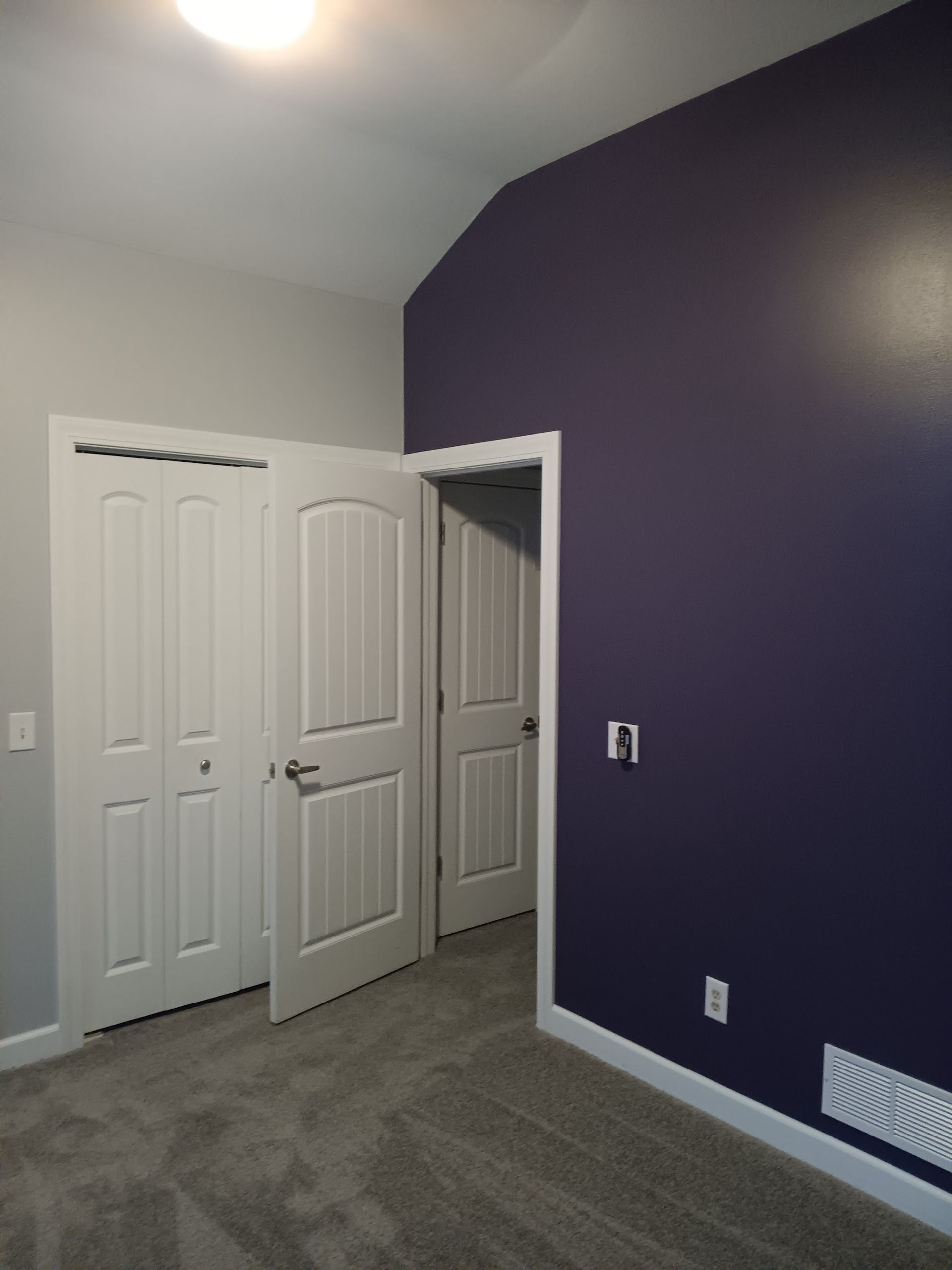 Bedroom with white doors, purple accent wall, and gray carpet.