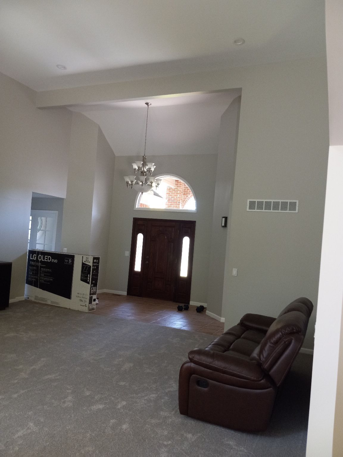 A living room with a high ceiling, chandelier, and dark brown leather recliner.