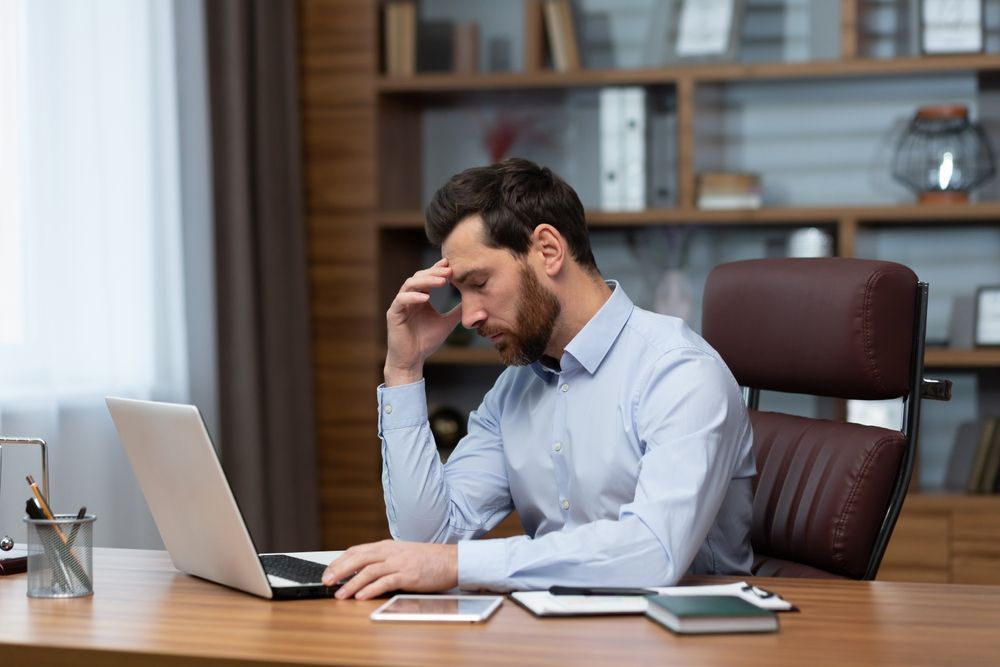 A Professional Sitting At A Desk With A Laptop, Resting A Hand On Their Forehead With An Expression Of Stress Or Focus — Australian Employee Lawyers in Broadbeach Waters, QLD