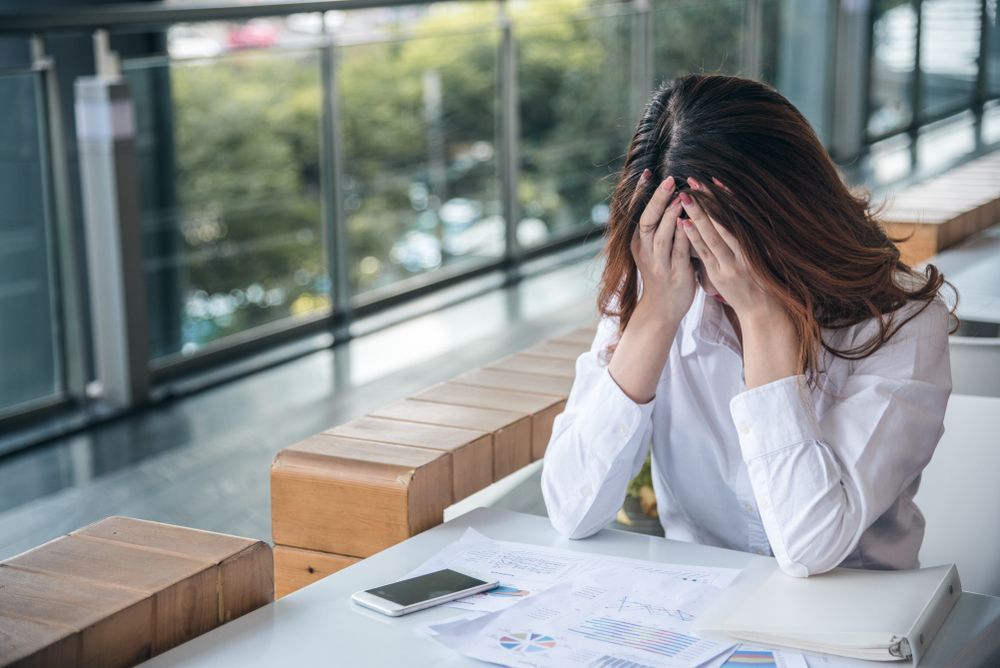 A Person in a White Shirt Sits at a Desk Holding Their Head and Distress — Australian Employee Lawyers in Broadbeach Waters, QLD
