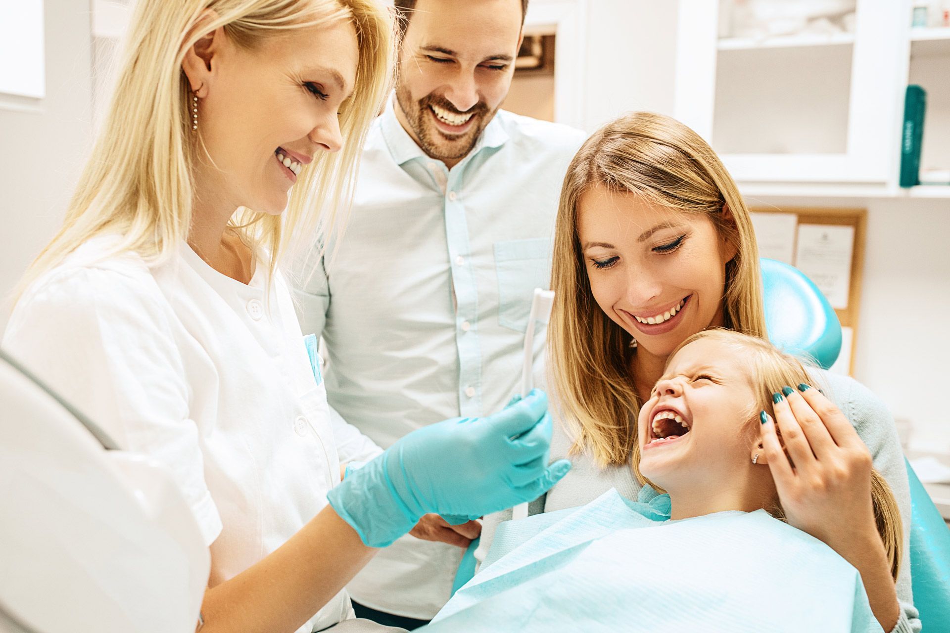Dental professional showing a toothbrush to a patient while another adult stands nearby.