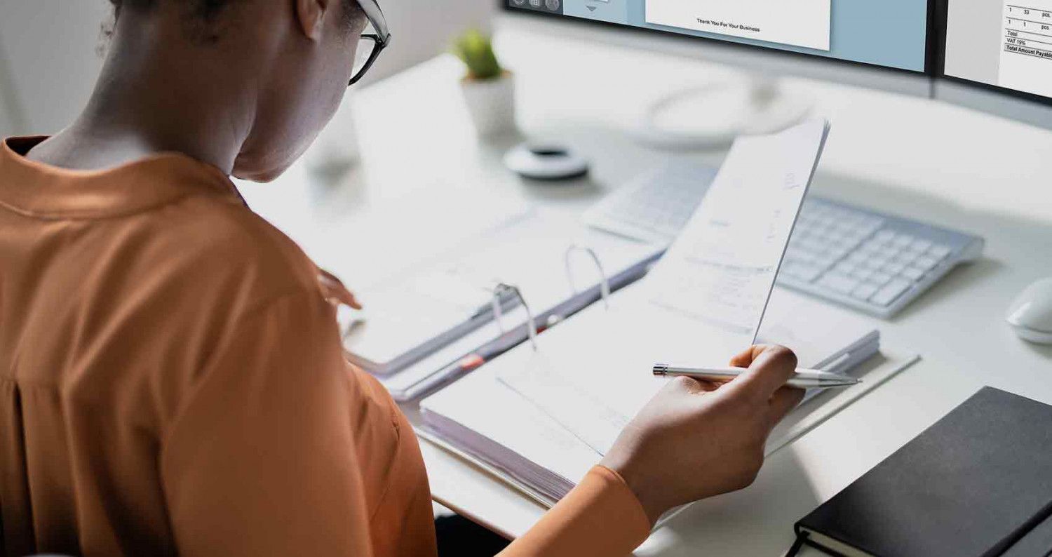 A woman is sitting at a desk looking at a piece of paper.