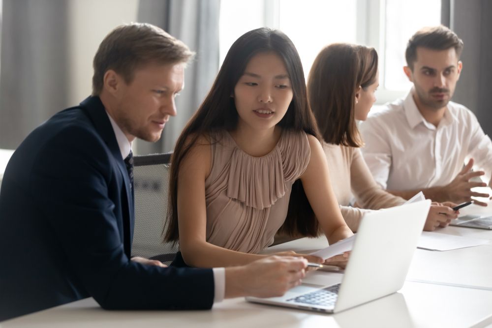 A group of people are sitting at a table looking at a laptop computer.