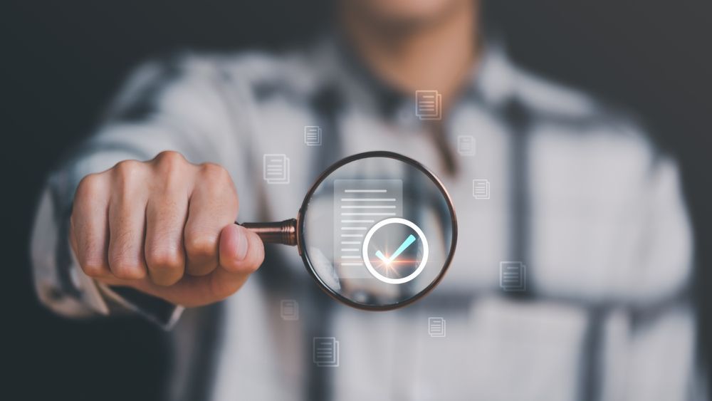 A man is holding a magnifying glass with a check mark on it.