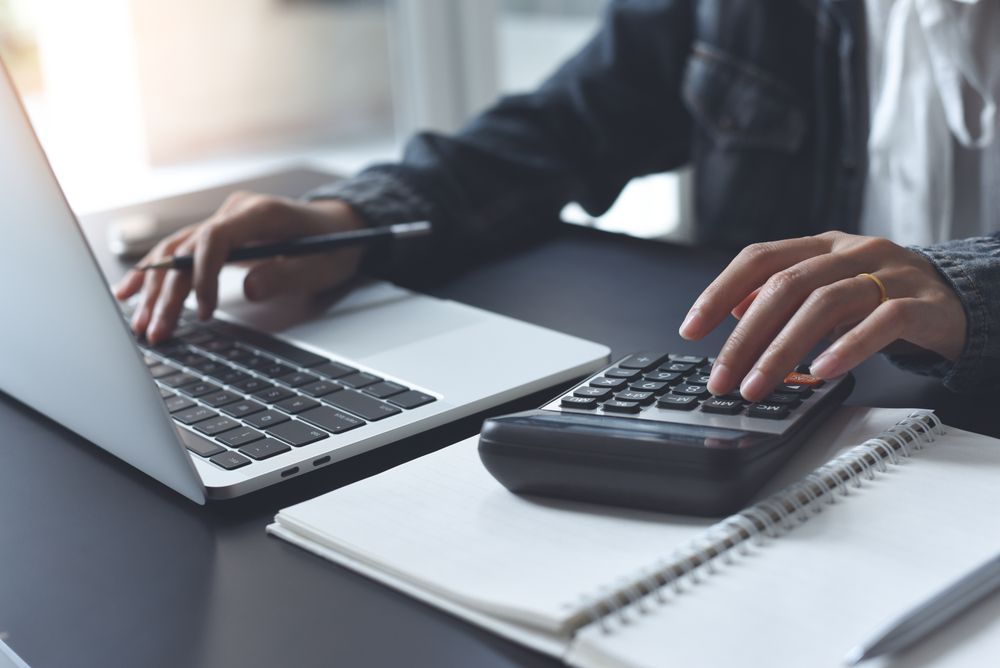 A pen is sitting on top of a pile of papers next to a calculator and glasses