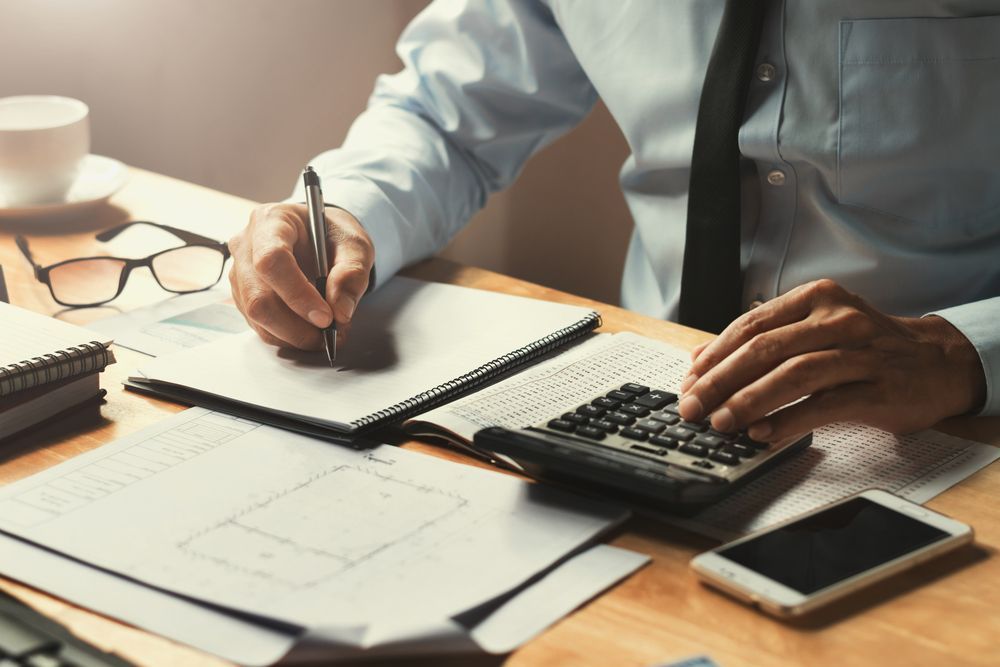 A pen is sitting on top of a pile of papers next to a calculator and glasses