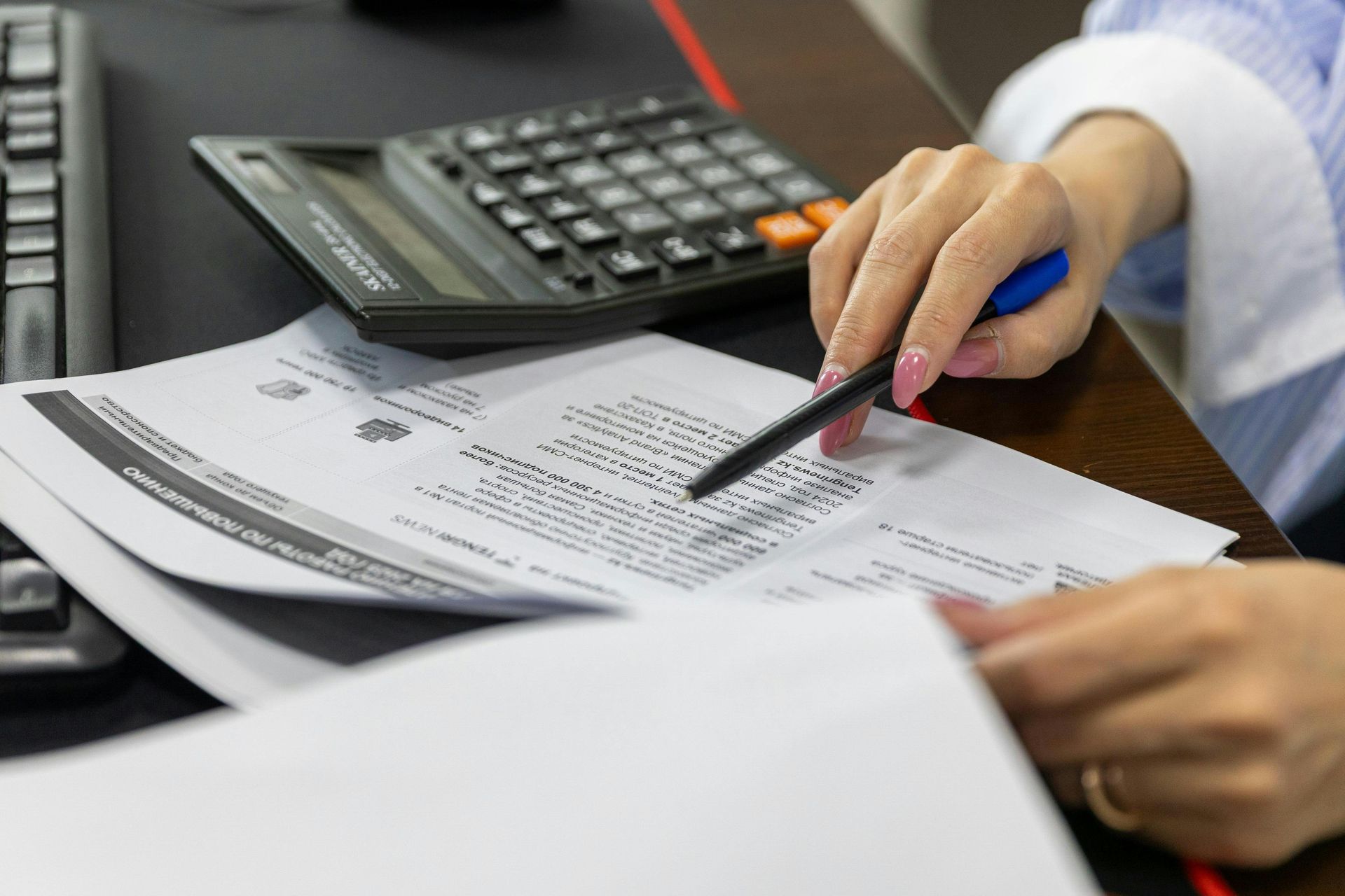 A woman is holding a pen over a piece of paper while using a calculator.
