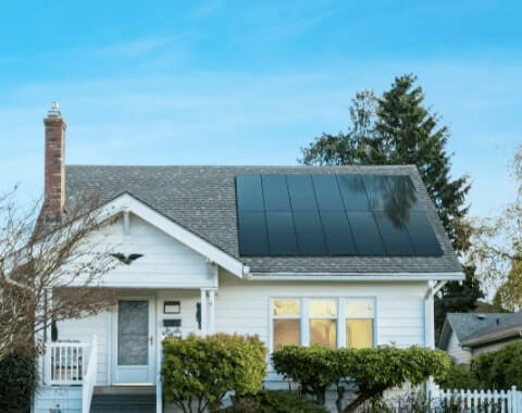 A white house with black solar panels on the roof.
