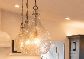 three clear glass pendant lights are hanging from the ceiling in a kitchen .