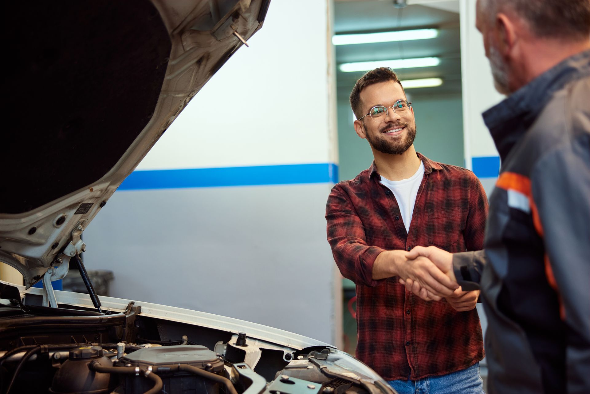 Man shaking hands with a uniformed mechanic  with a car hood opened.