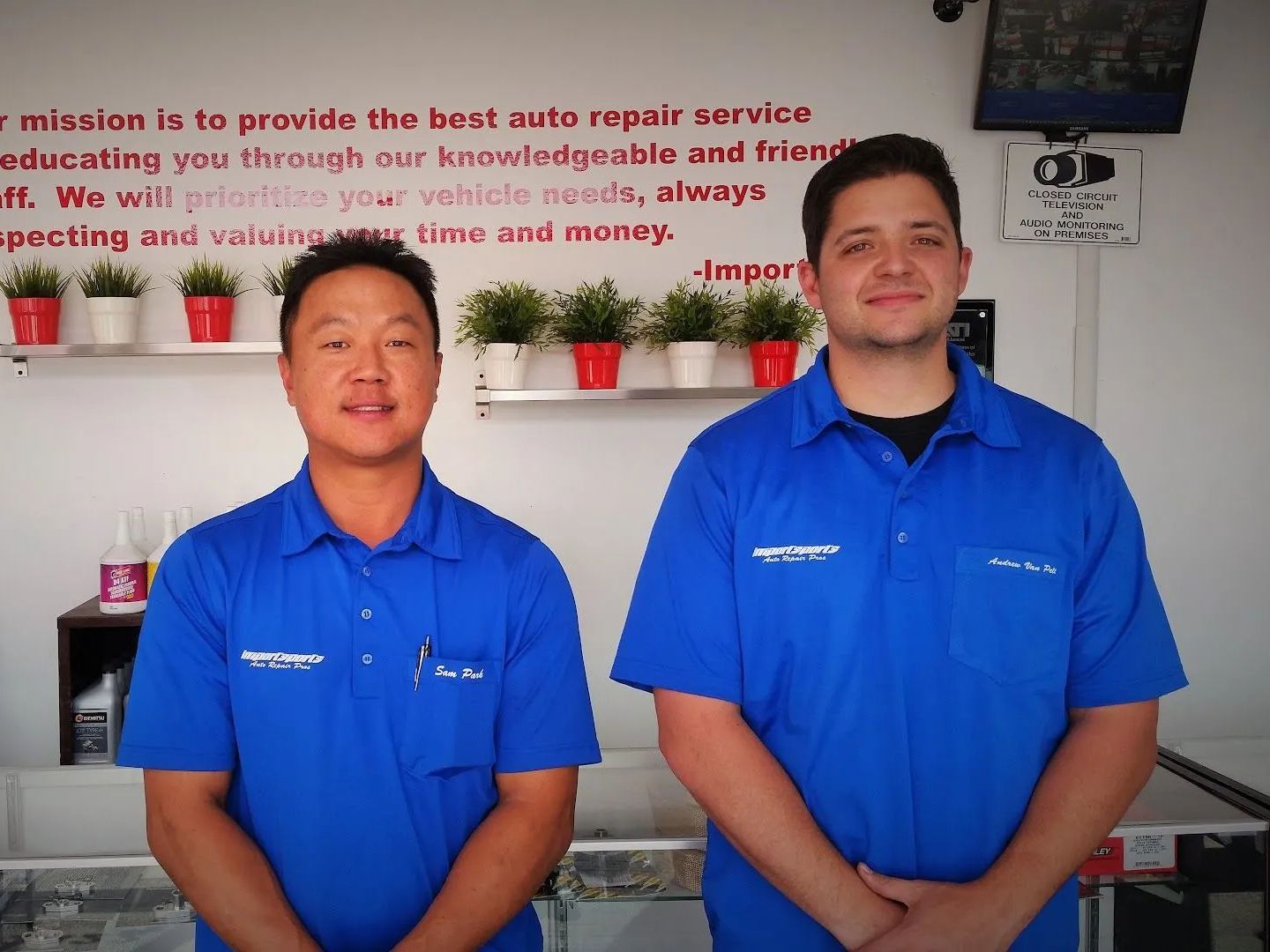 Two men in blue shirts stand in front of a wall with text. | Importsports