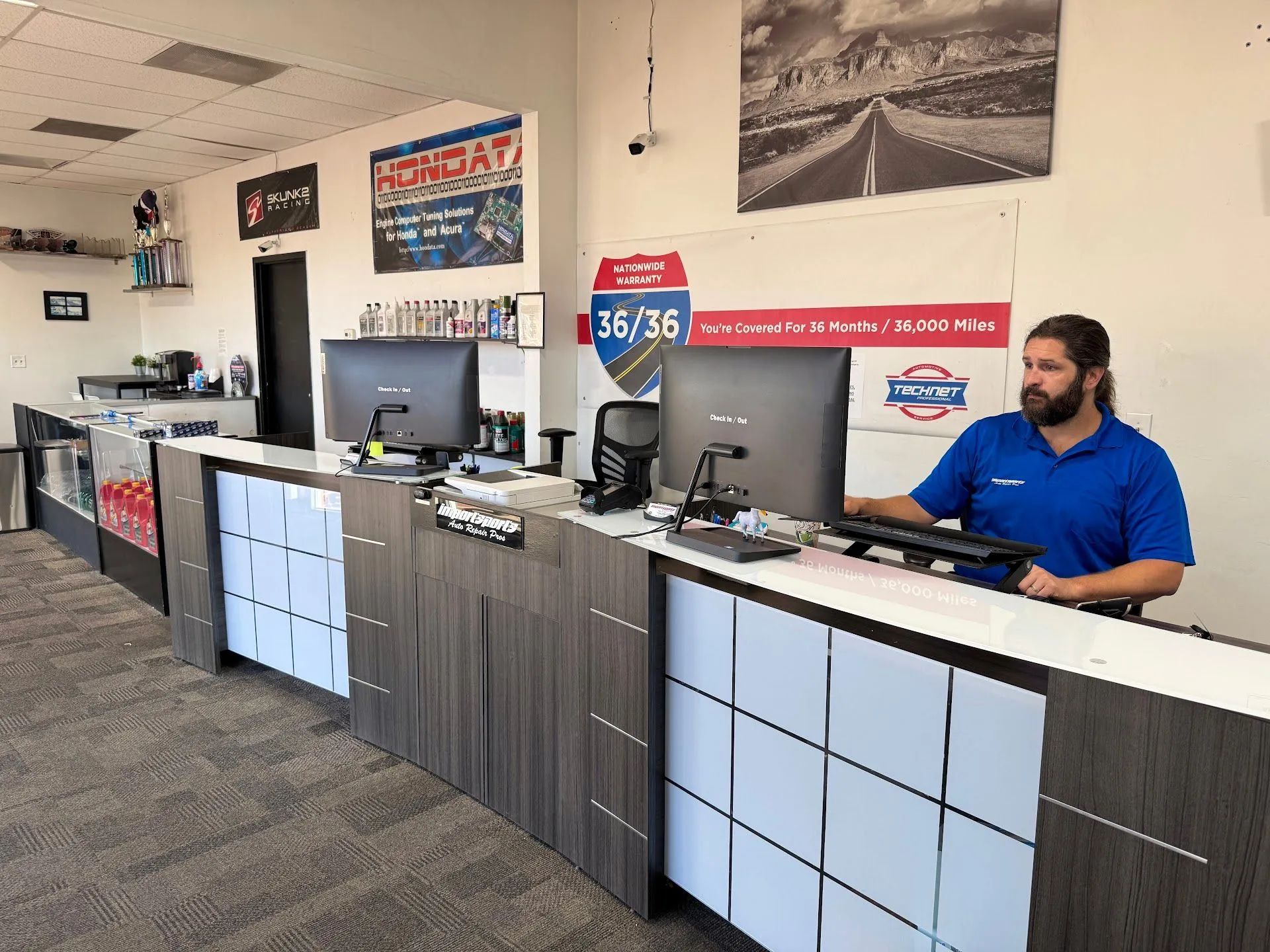 A man at a computer behind a counter in an office setting. | Importsports