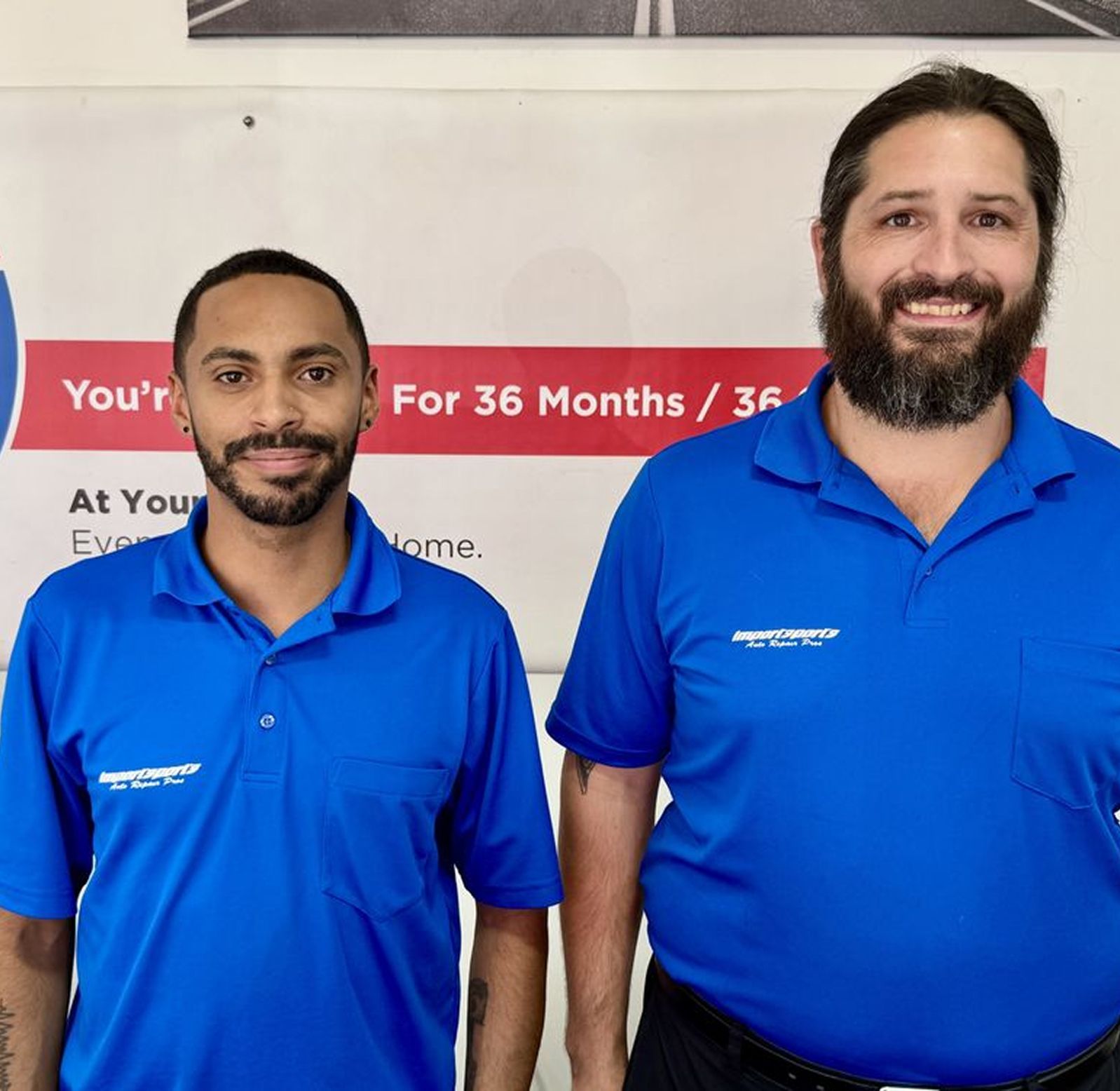 Two silver cars in a garage. One is up on a lift. A red metal scaffolding is in the middle of the frame. | Importsports