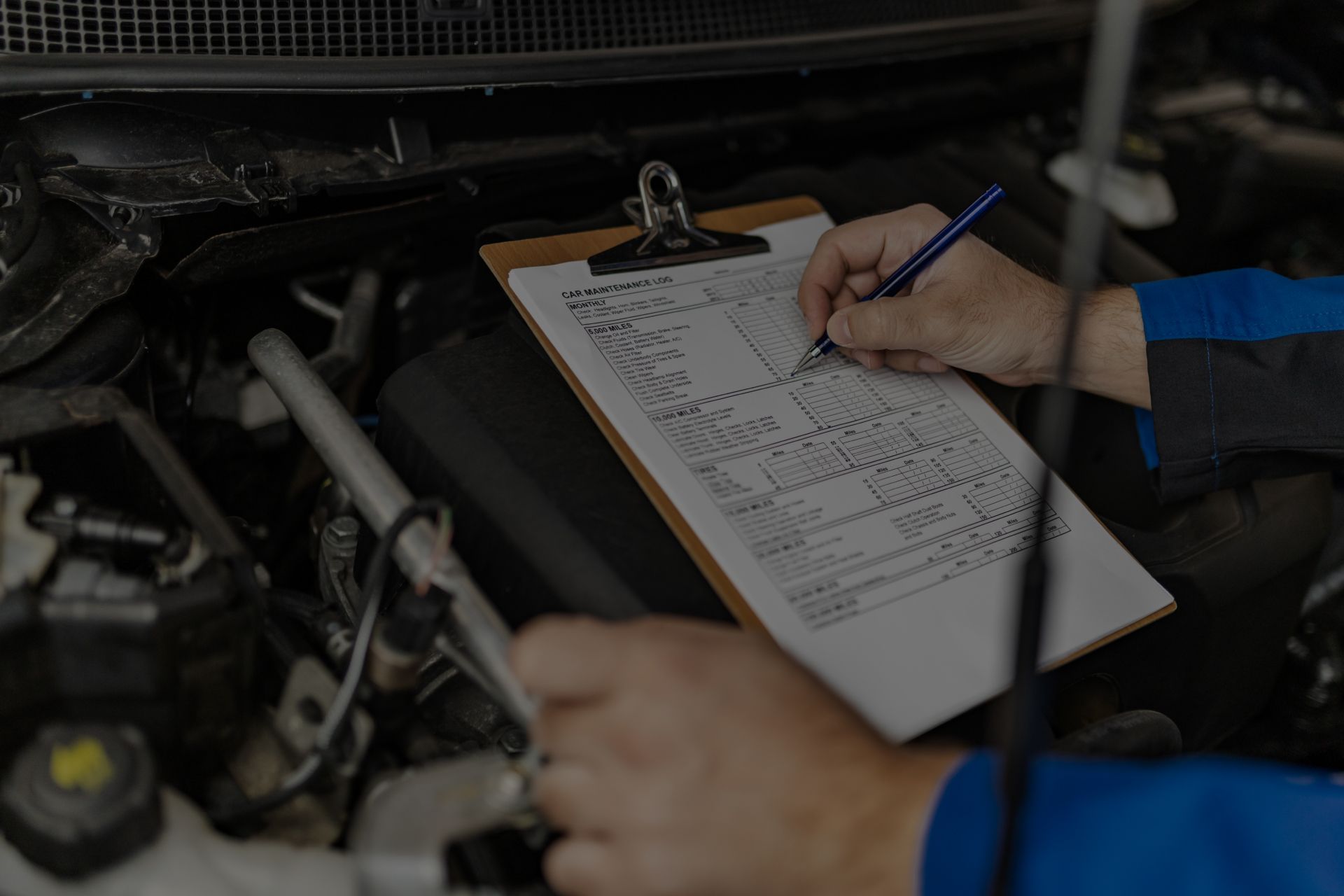 Mechanic writing on a clipboard while inspecting a car engine. | Importsports