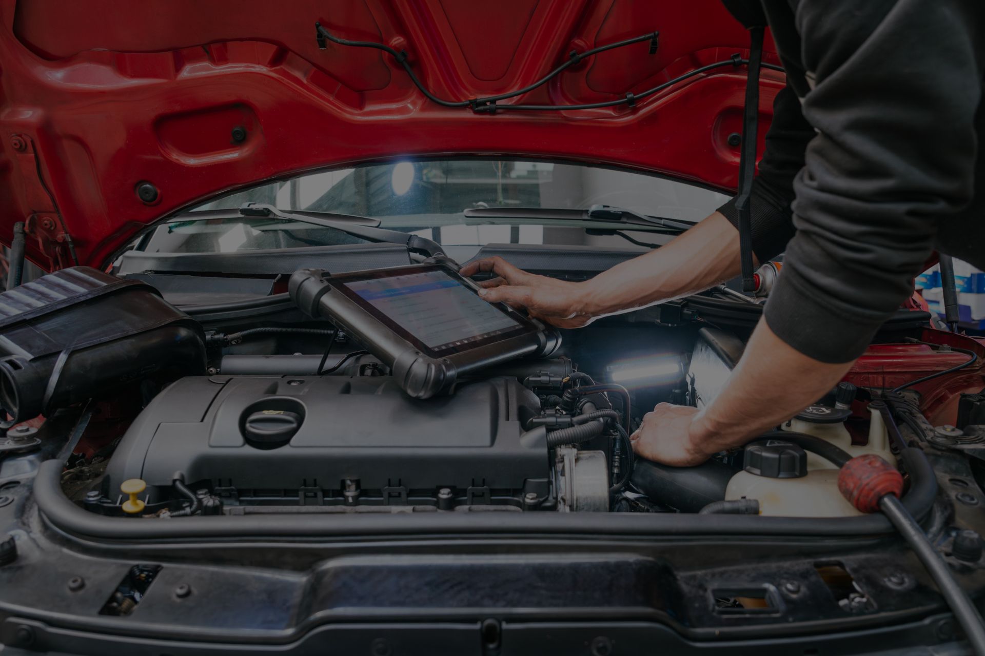 Mechanic using diagnostic tool on a car engine under the hood. Red car, interior setting. | Importspor