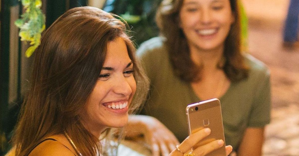 Two women are sitting at a table looking at a cell phone.