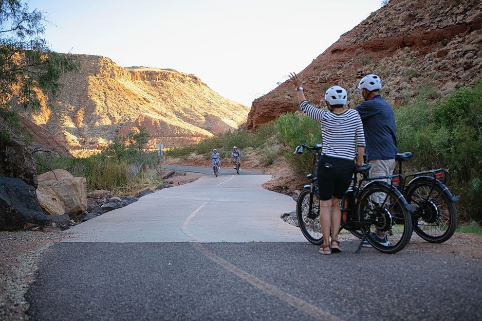 A couple wave to their fellow ebike riders on a paved bike trail.