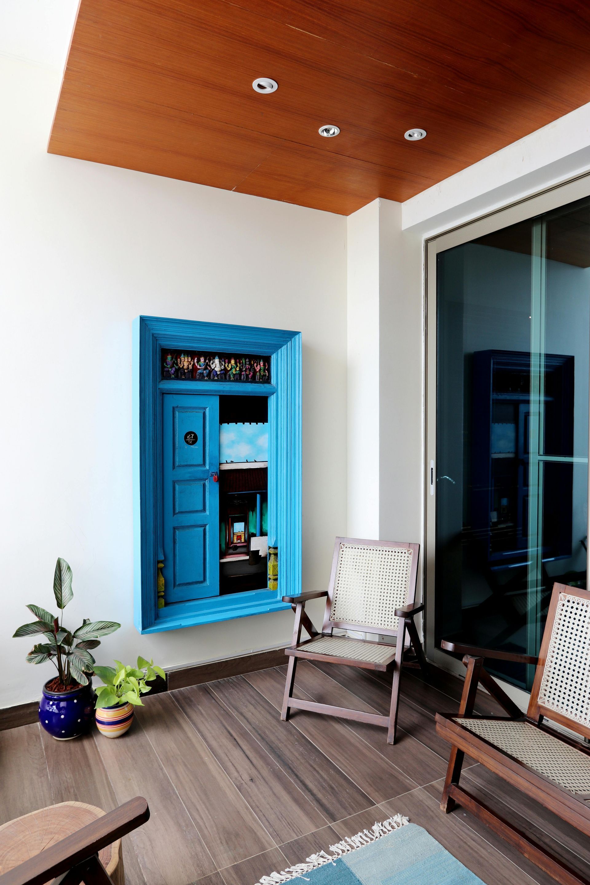 Blue cabinet on white wall of an outdoor seating area, wood ceiling and floor, with chairs and plants.