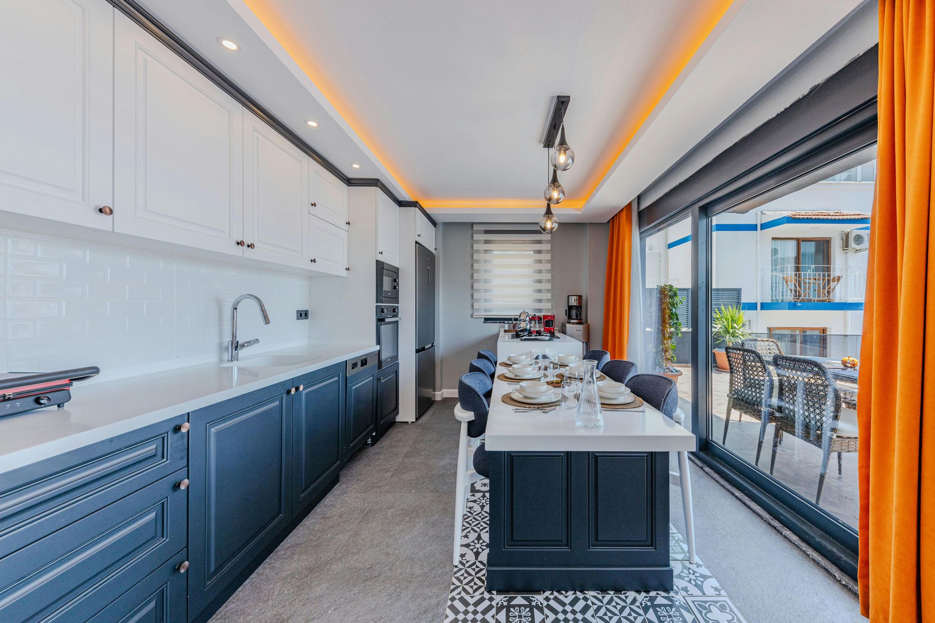 Kitchen with white cabinets, blue lower cabinets, island, dining set, and an outdoor view.