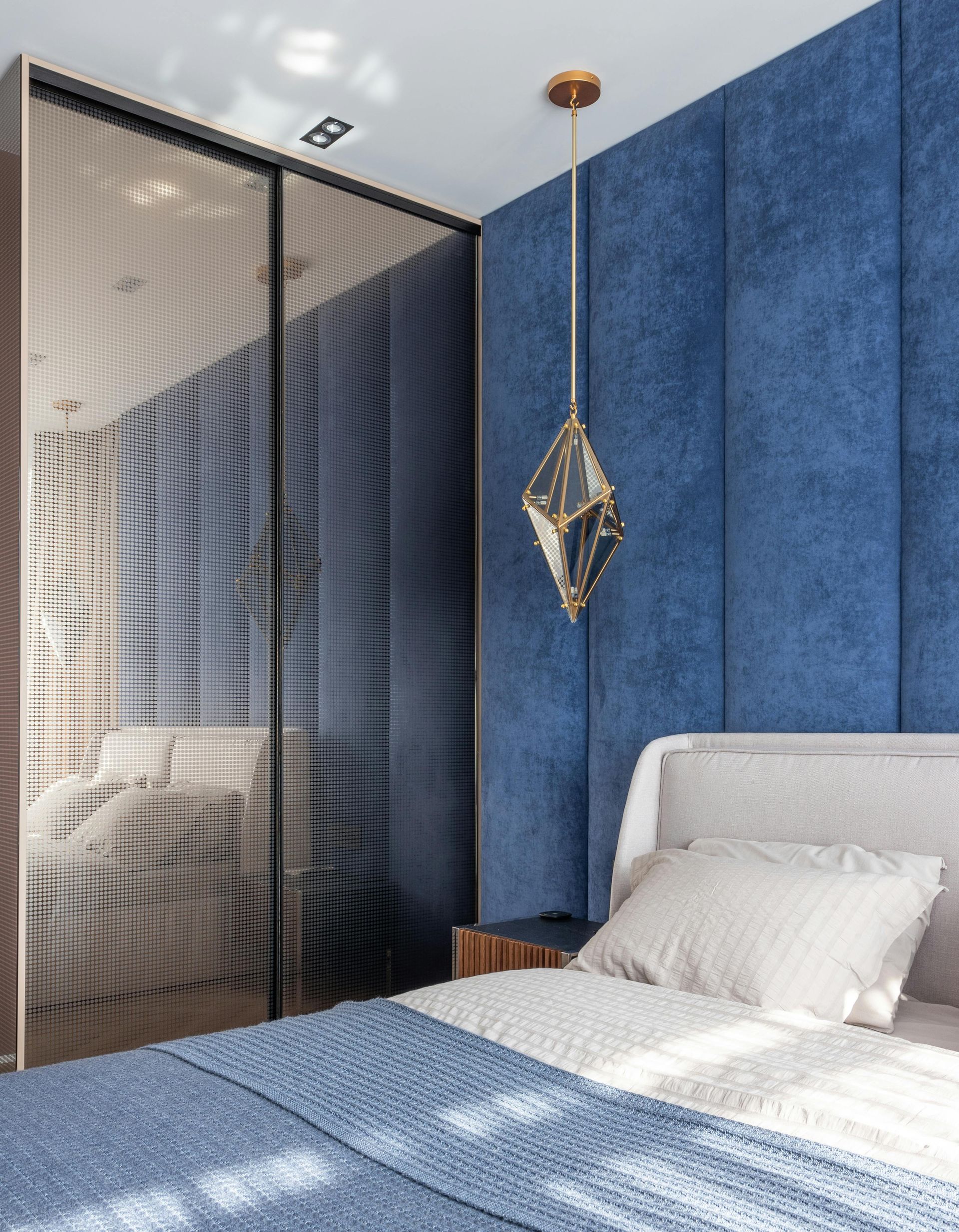 Bedroom with blue upholstered headboard, bed, pendant light, and closet.