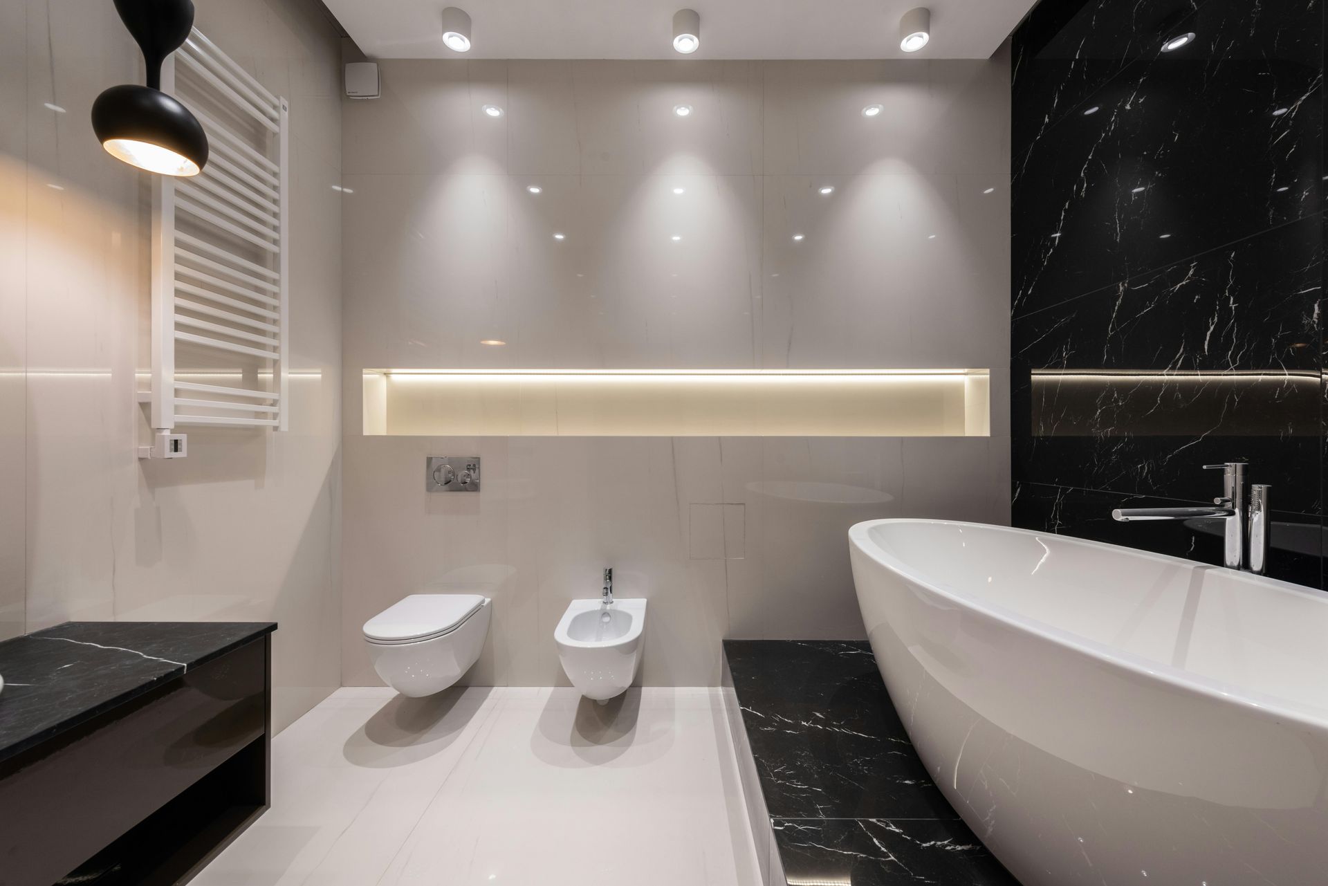 Modern bathroom with a white tub, black marble accents, and bright overhead lights.