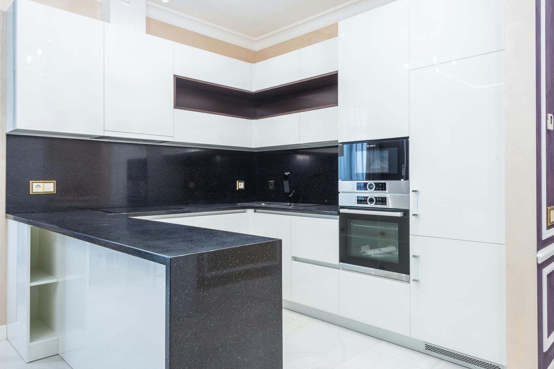 Modern white kitchen with black countertops and built-in appliances.