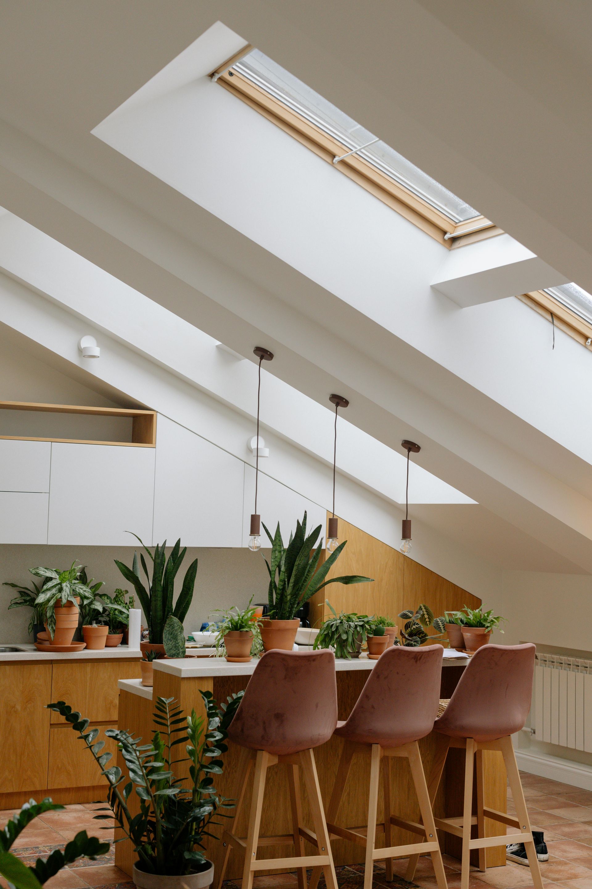 Kitchen with slanted ceiling, skylights, and a bar with pink stools, plants.