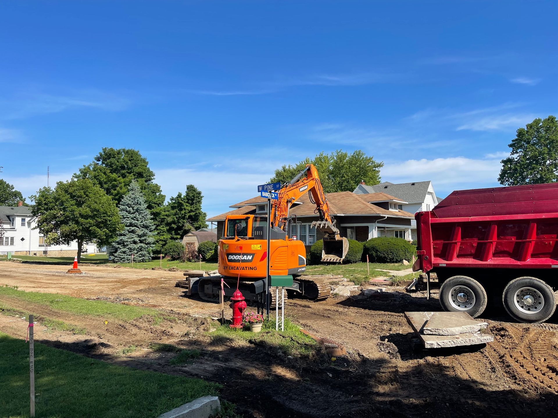 Orange excavator loading a white dump truck with dirt at a construction site.