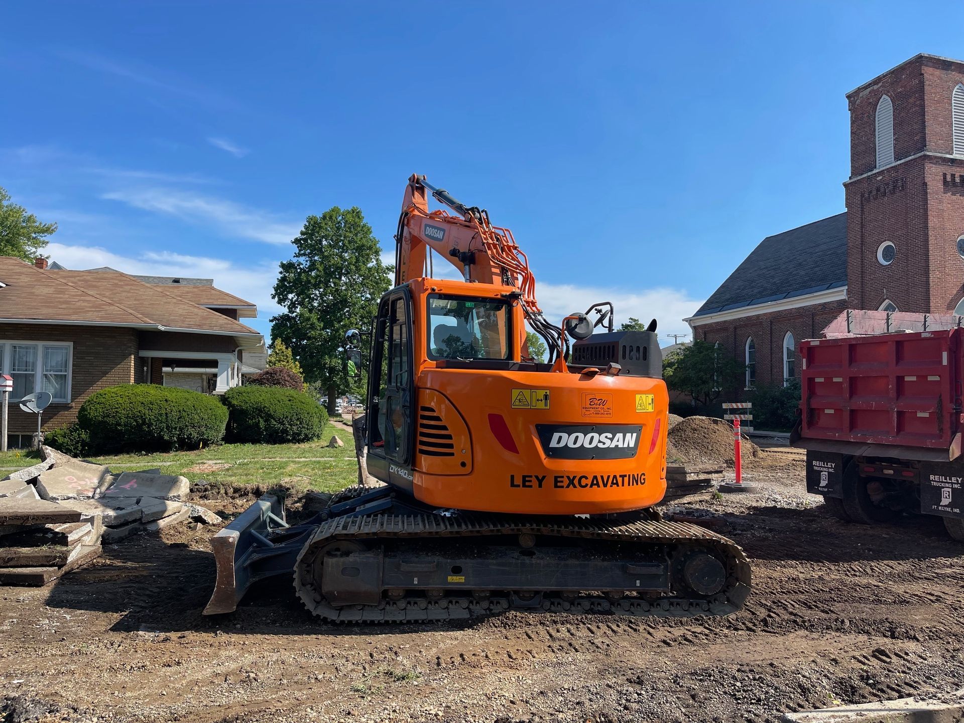 Yellow excavator digging into a reddish-brown earth mound at a construction site.