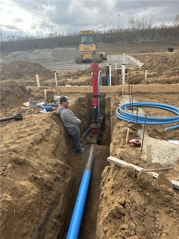Road excavation revealing buried yellow and blue pipes; green pipe on surface.