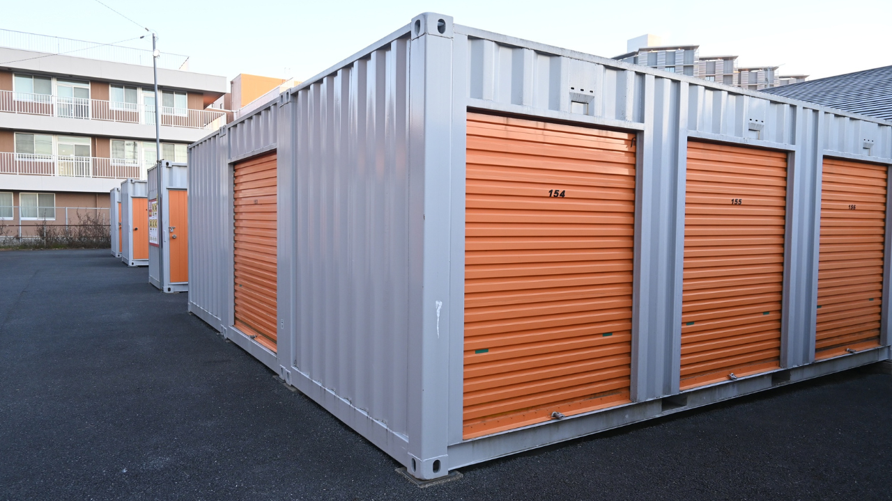 Rows of gray and orange storage units in an outdoor parking area, near a building.