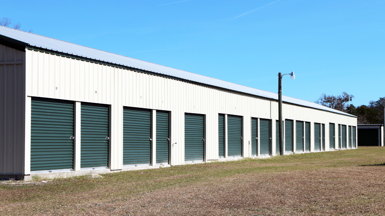 Row of green storage unit doors under a white metal building with blue sky.