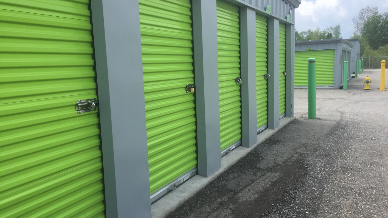 Bright green storage unit doors in a row, with gray pillars and a paved pathway.