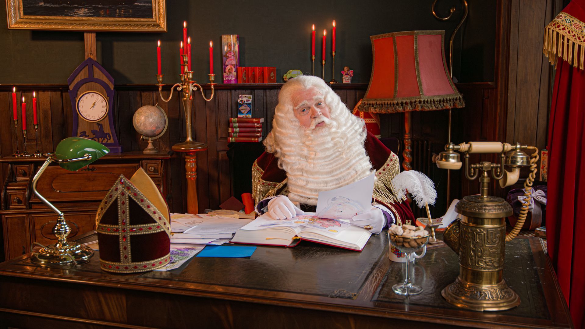 Sinterklaas zit aan een donkerhouten bureau en bekijkt documenten in een kamer die is versierd