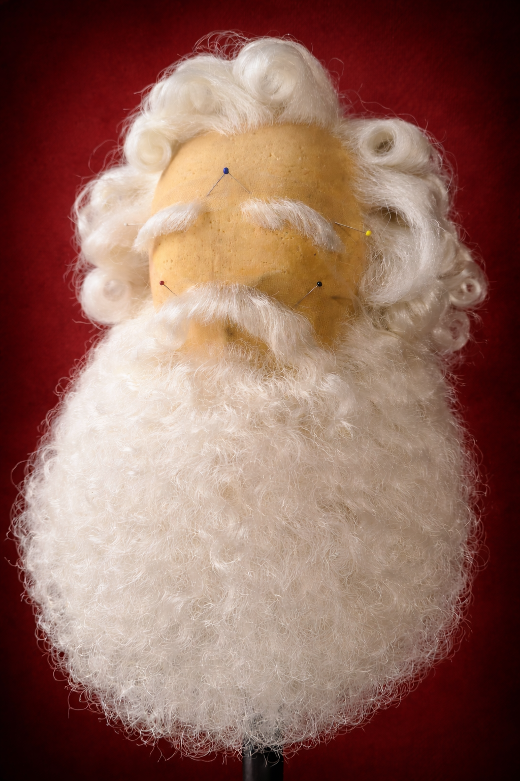 Een figuur van een kerstmanhoofd met een wollen baard en wit haar, tegen een rode achtergrond.