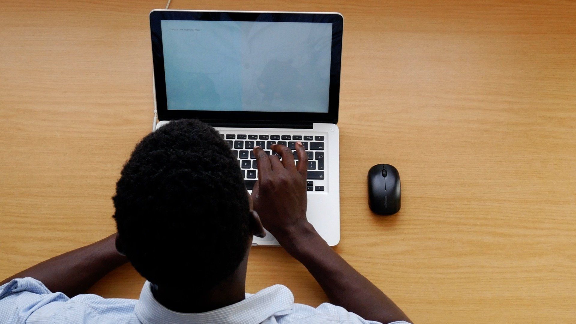a black man is typing on a laptop with a mouse next to him