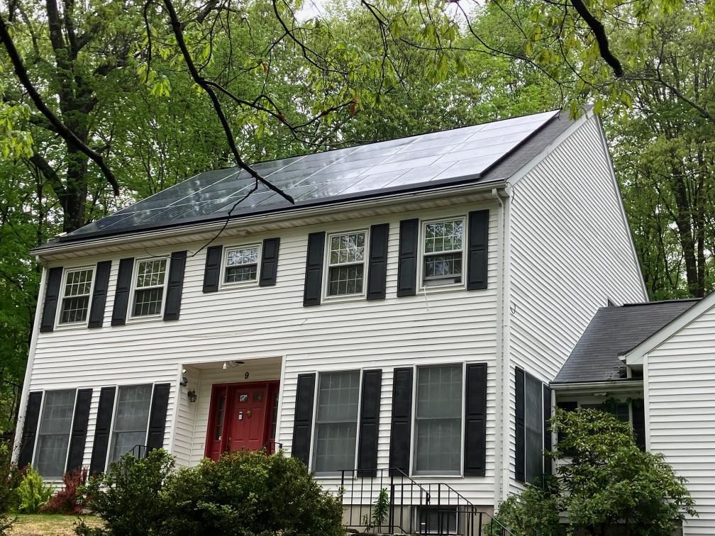 A white house with black shutters and solar panels on the roof.