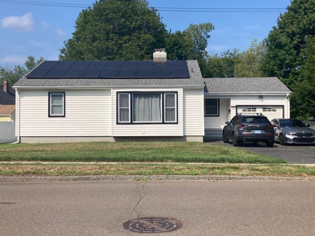 Two cars are parked in front of a house with solar panels on the roof.