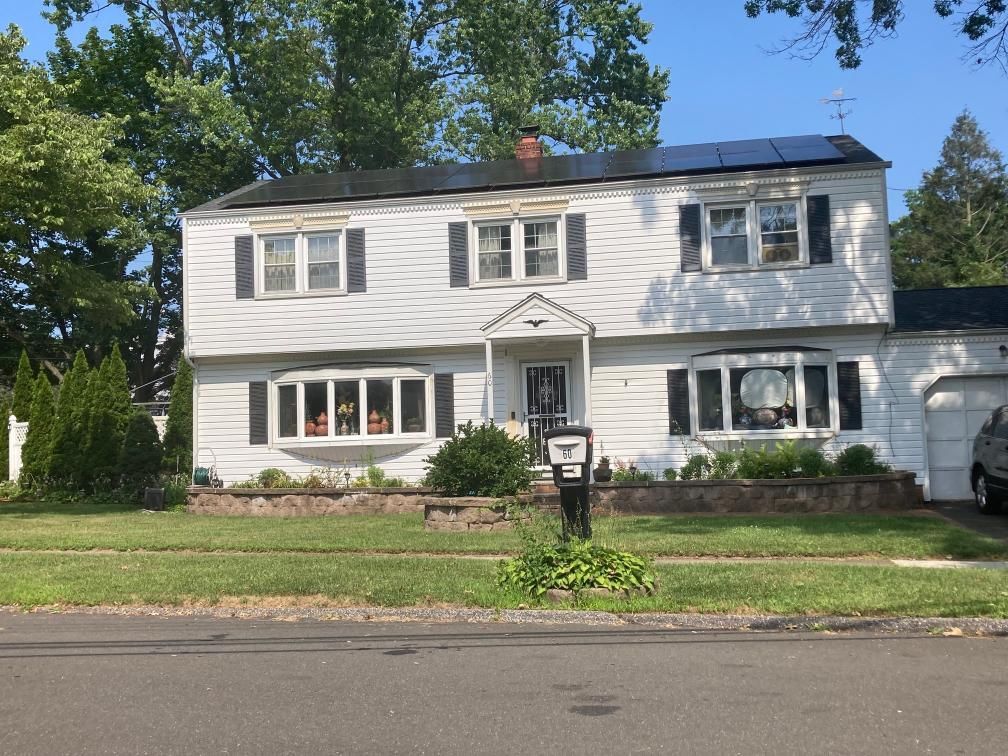 A white house with black shutters and solar panels on the roof.